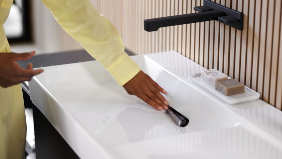 Woman removes comb insert on Geberit ONE washbasin with tap in black matt. (© Geberit)