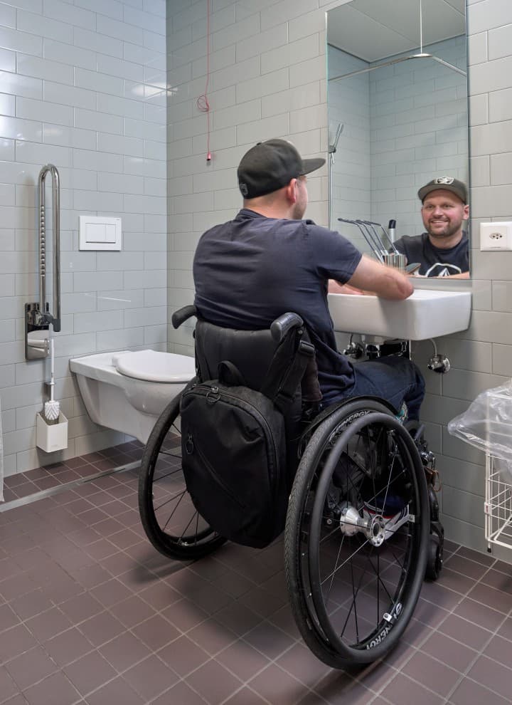 Peter Roos in a wheelchair at the washbasin area in a barrier-free bathroom (© Ben Huggler) Peter Roos in a wheelchair at the washbasin area in a barrier-free bathroom (© Ben Huggler)